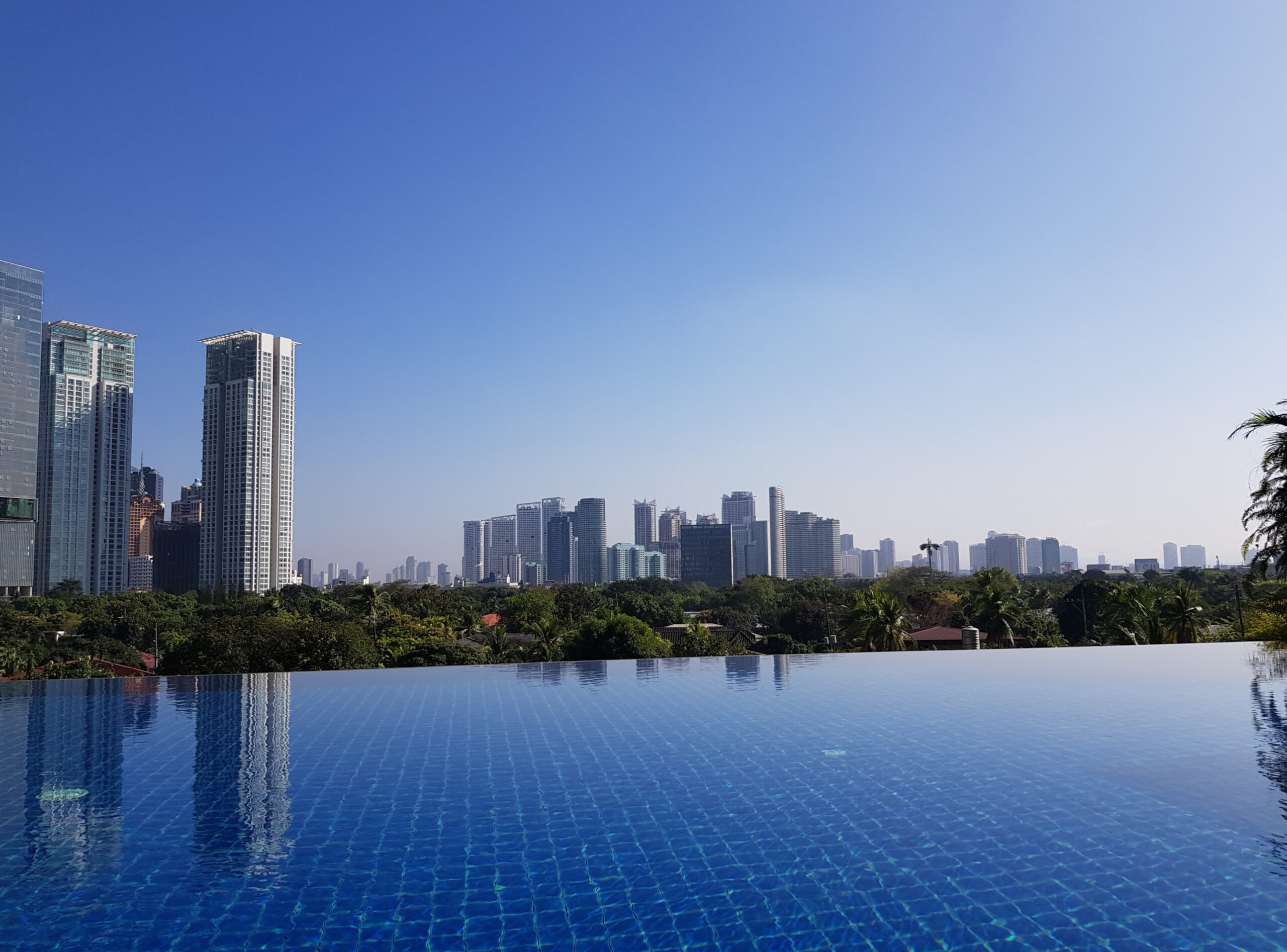 Manila skyline in the Philippines with skyscrapers and an infinity pool in the foreground under a clear sky