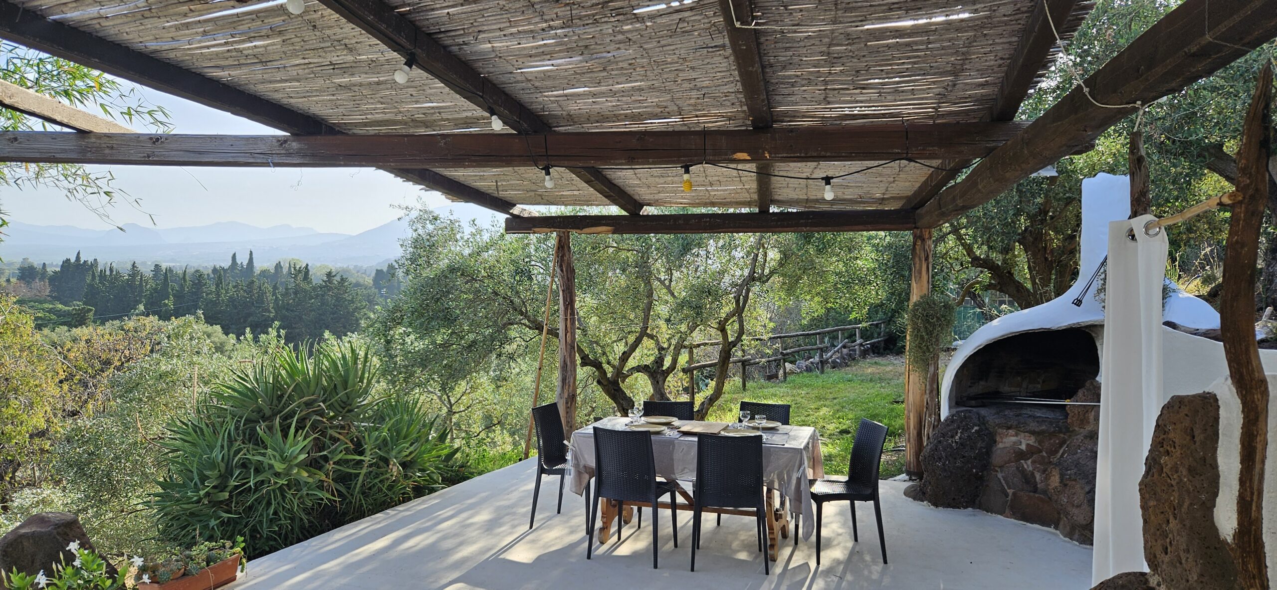 Outdoor dining in Sardinia, set table under pergola with olive grove and mountain view