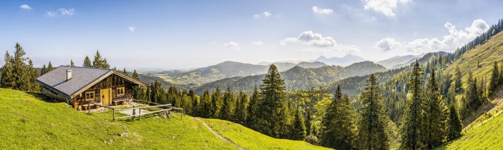 Berghütte auf Almwiese mit Blick über bewaldete Berge und Tal