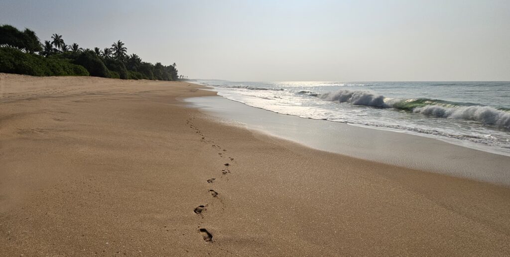 Tropischer Strand mit Fußspuren im Sand, Palmen und sanften Wellen